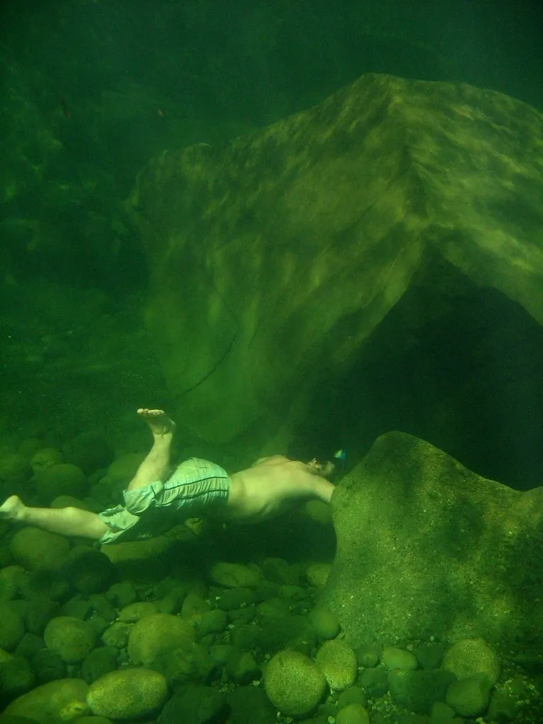 Fotografia subaquática original sem edição: Nadadora sob uma saliência de pedras